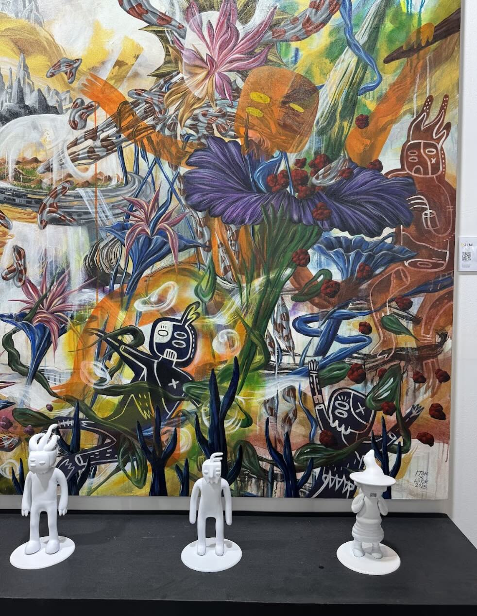 Lukisan penuh warna bertema flora, fauna, dan karakter imajinatif dengan tiga figur patung putih mini di bagian depan, karya seniman kontemporer yang dipamerkan di ArtMoments Jakarta 2025.
